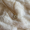 Gold necklace with a circular pendant featuring the letter 'A' on a white fluffy surface.