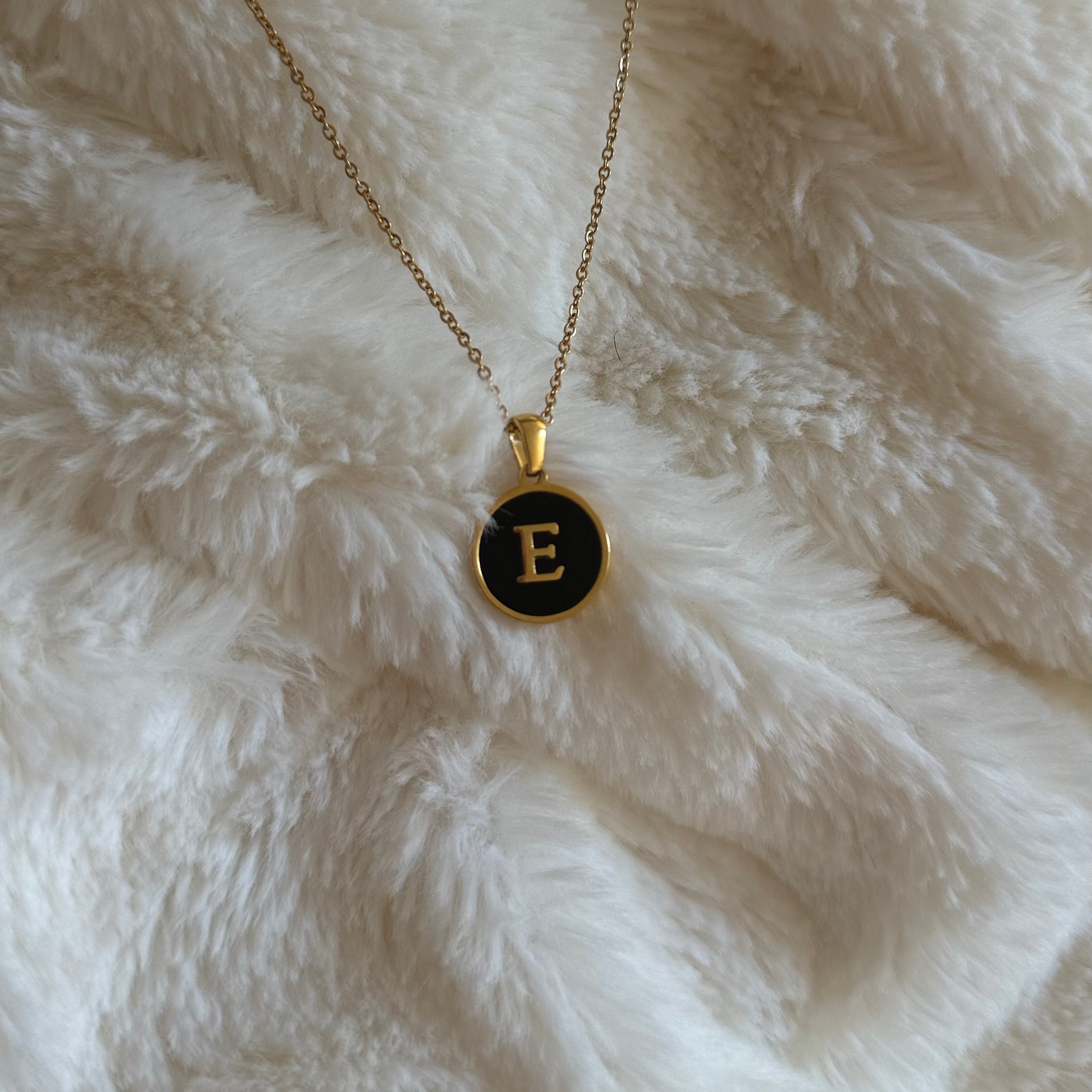 Necklace with a black pendant featuring the letter 'E' on a white fluffy surface