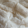Gold necklace with a 'H' pendant on a white fluffy surface