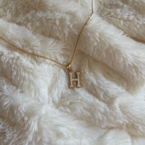 Gold necklace with a 'H' pendant on a white fluffy surface