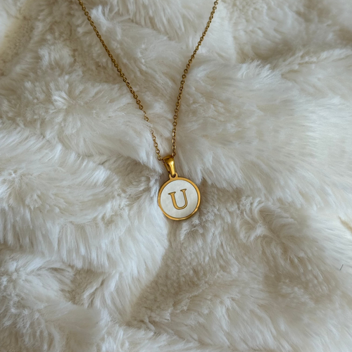 Gold necklace with a 'U' pendant on a white fluffy surface