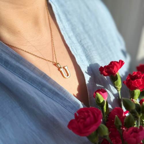 Person wearing a gold necklace with a 'U' pendant, holding red flowers.