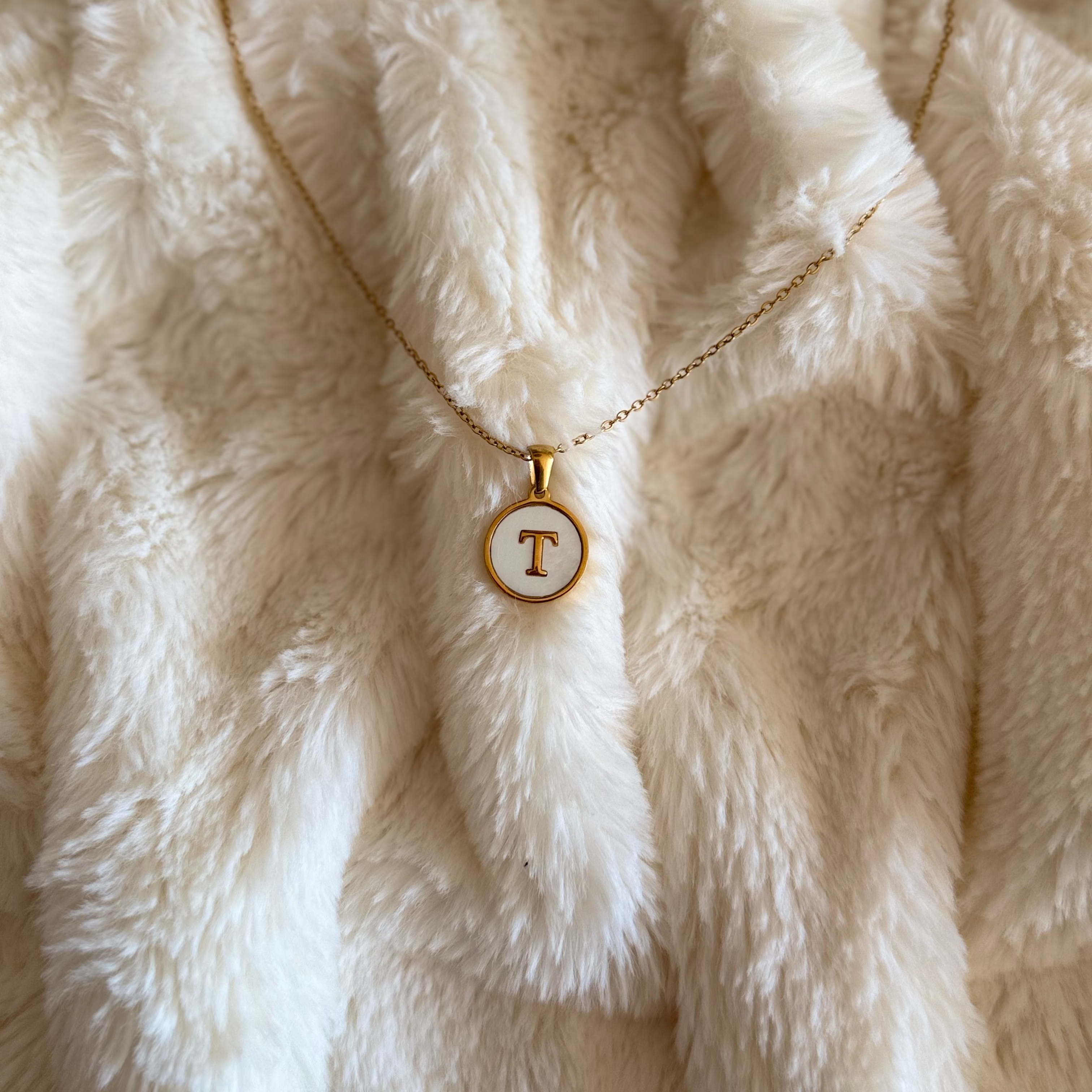 Necklace with a circular pendant featuring the letter 'T' on a fluffy white surface